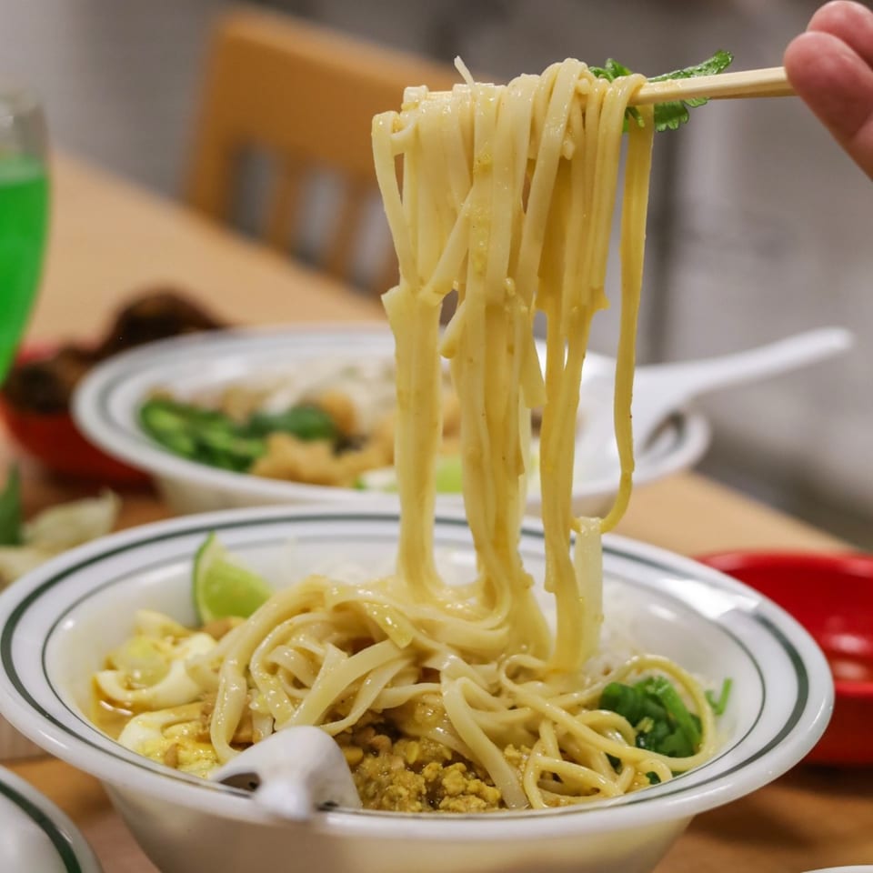 Chopsticks lifting creamy yellow noodles from a bowl with lime and ground meat.