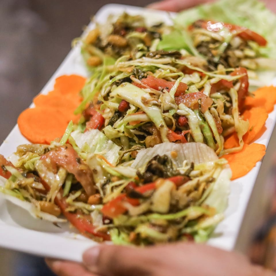 A person holding a white platter with several servings of fresh green salad with tomatoes and carrots.