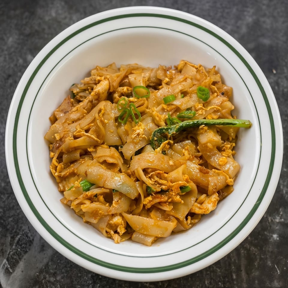 A white bowl with green stripes filled with Pad See Ew noodles, scrambled egg, and green onions.