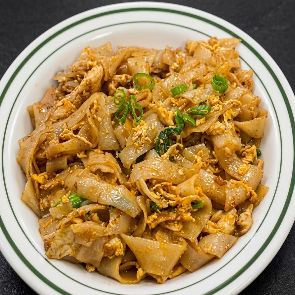 Close-up of a white bowl with green stripes filled with Pad See Ew noodles, chicken, and egg.